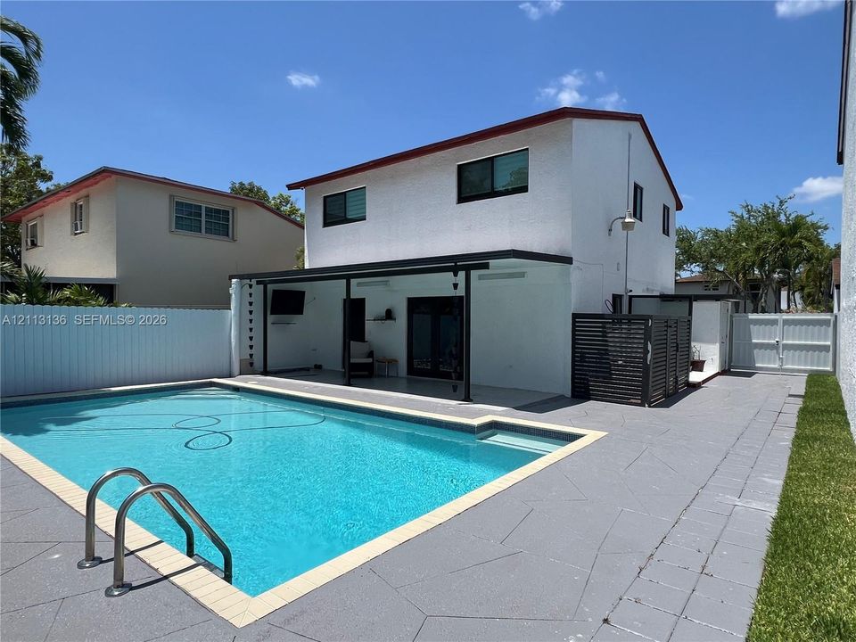 In-ground swimming pool with surrounding patio, covered outdoor area, and privacy fencing