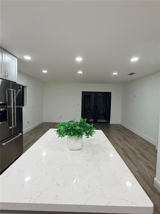 Kitchen island with a light-toned, veined countertop, stainless steel refrigerator, recessed lighting, and wood-finish flooring