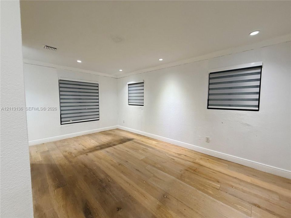 Interior space featuring wood-finish flooring, neutral wall tones, recessed lighting, and dual-layered window shades