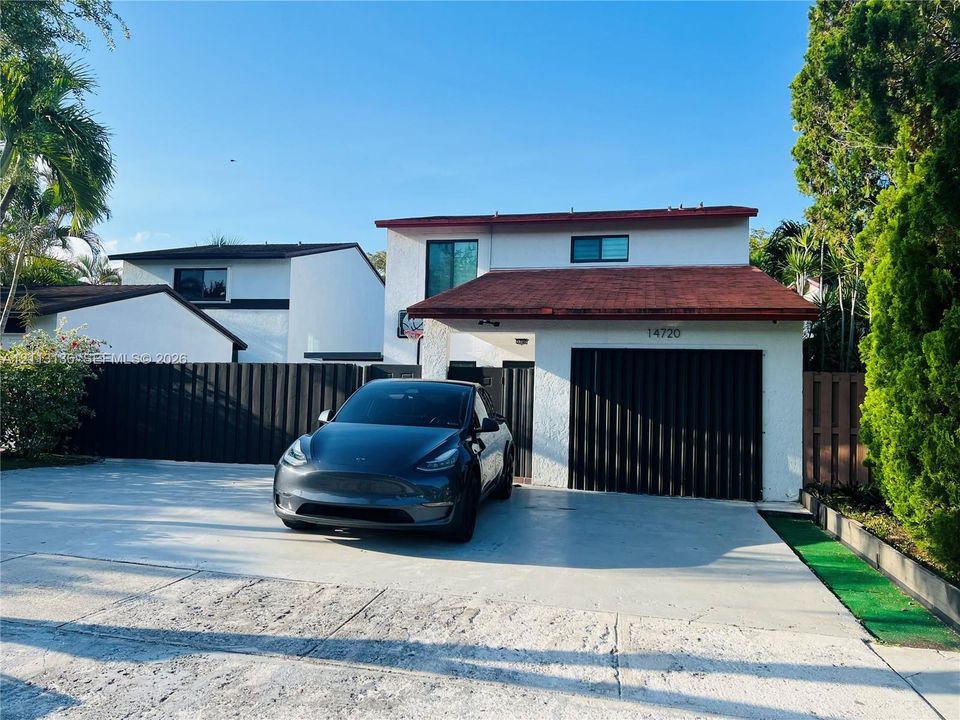 Two-story exterior featuring a concrete facade, a shingled roof, a vertical-slat garage door, and a private concrete driveway
