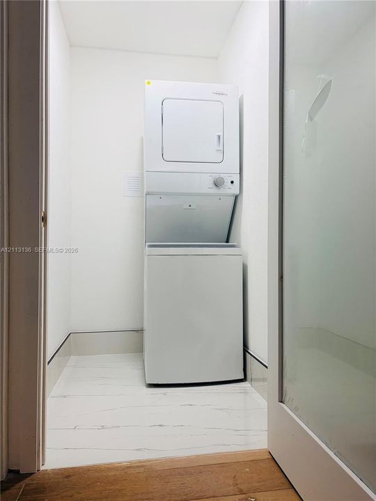 Laundry area featuring a stackable washer and dryer unit, white walls, and white flooring with charcoal veining