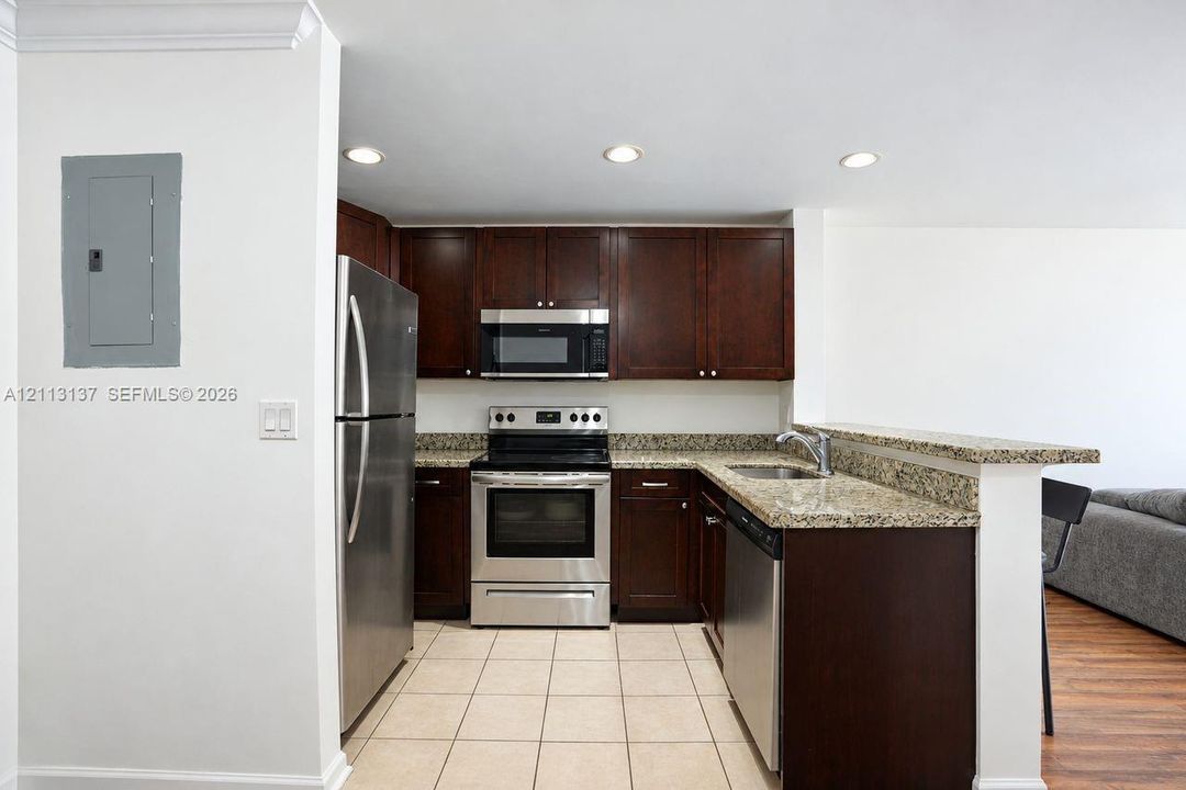 Kitchen featuring dark wood cabinetry, stone countertops, stainless steel appliances, and tiled flooring