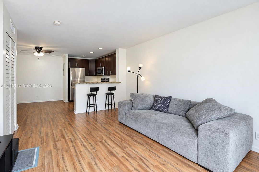Open-concept interior featuring wood-finish flooring, dark wood cabinetry, stainless steel kitchen appliances, stone-surface breakfast bar, and recessed lighting
