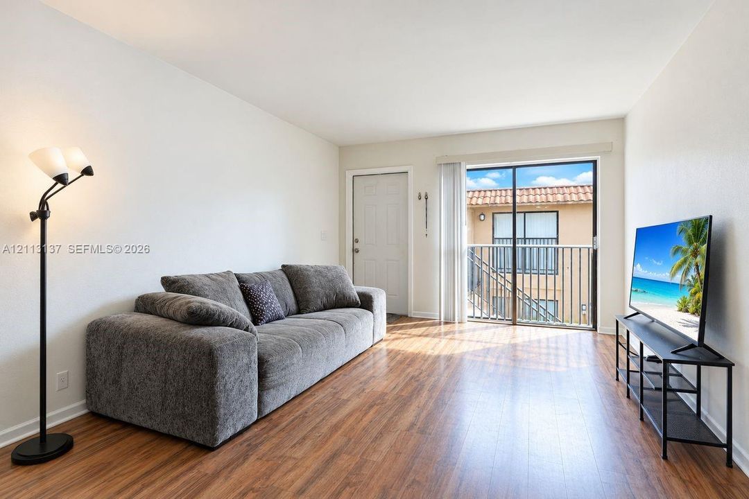 Living area featuring wood-finish flooring, neutral wall paint, and a sliding glass door providing access to a private balcony with a metal railing