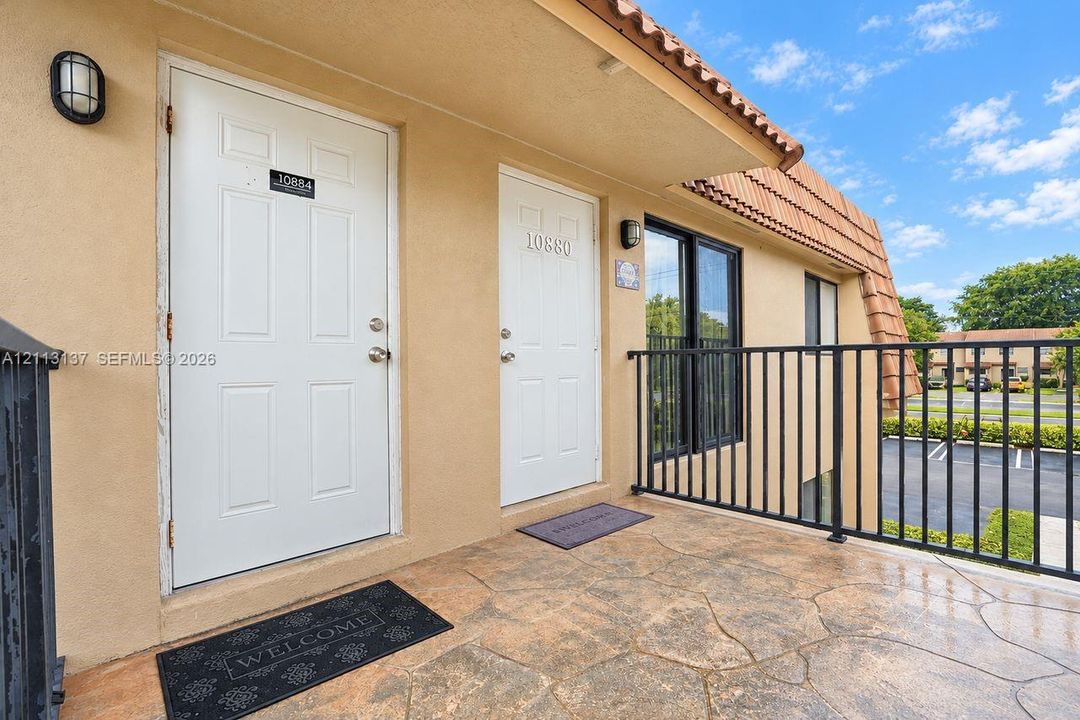 Exterior walkway featuring a stamped concrete surface, black metal railing, and light-toned stucco wall finish