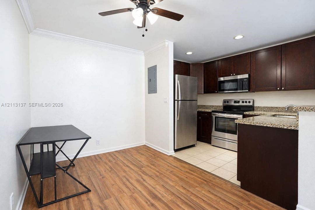 Kitchen featuring dark wood cabinetry, stone-finish countertops, stainless steel appliances, tile flooring, and wood-finish flooring