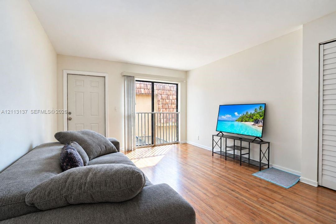 Living area featuring wood-finish flooring, neutral wall paint, and a sliding glass door providing access to a metal-railed balcony