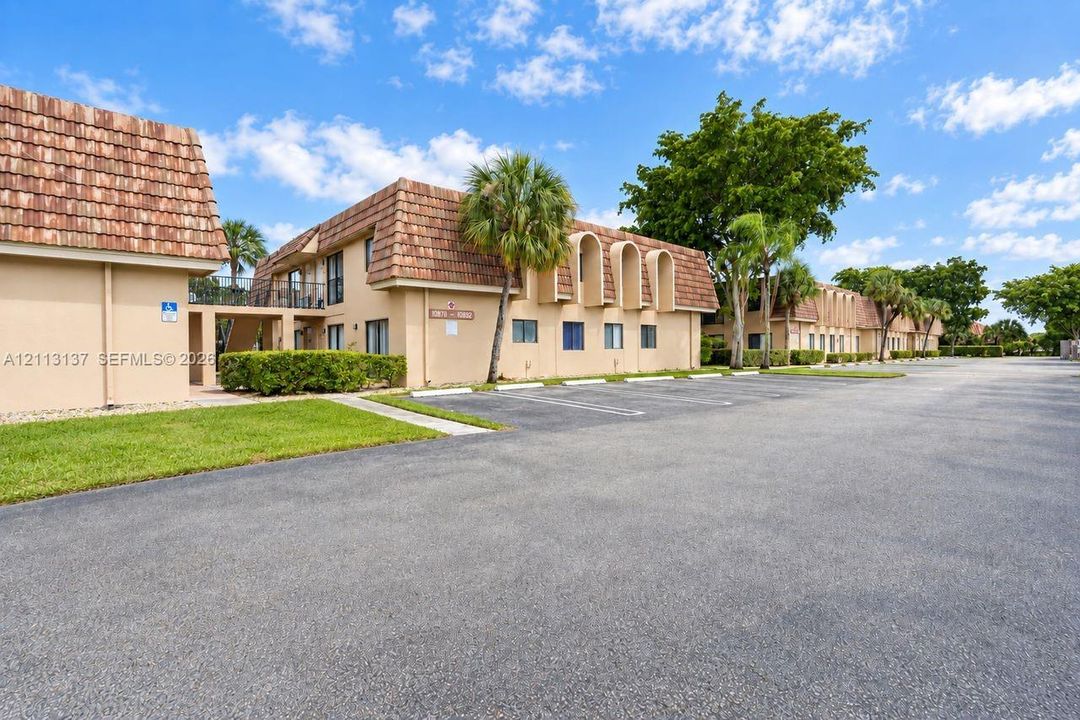 Two-story exterior featuring a clay tile roof, arched architectural details, stucco siding, paved parking area, and landscaped grounds