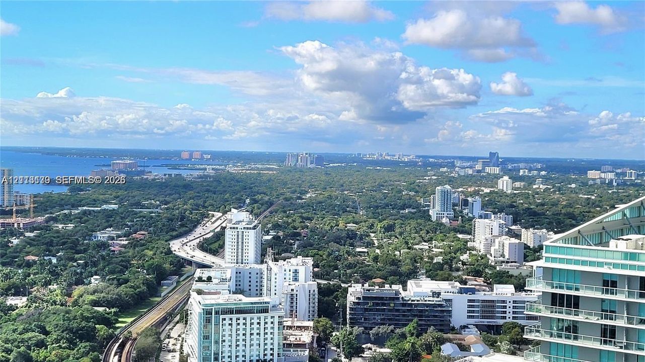 High-altitude perspective featuring coastal water scenery, expansive greenery, and urban cityscape