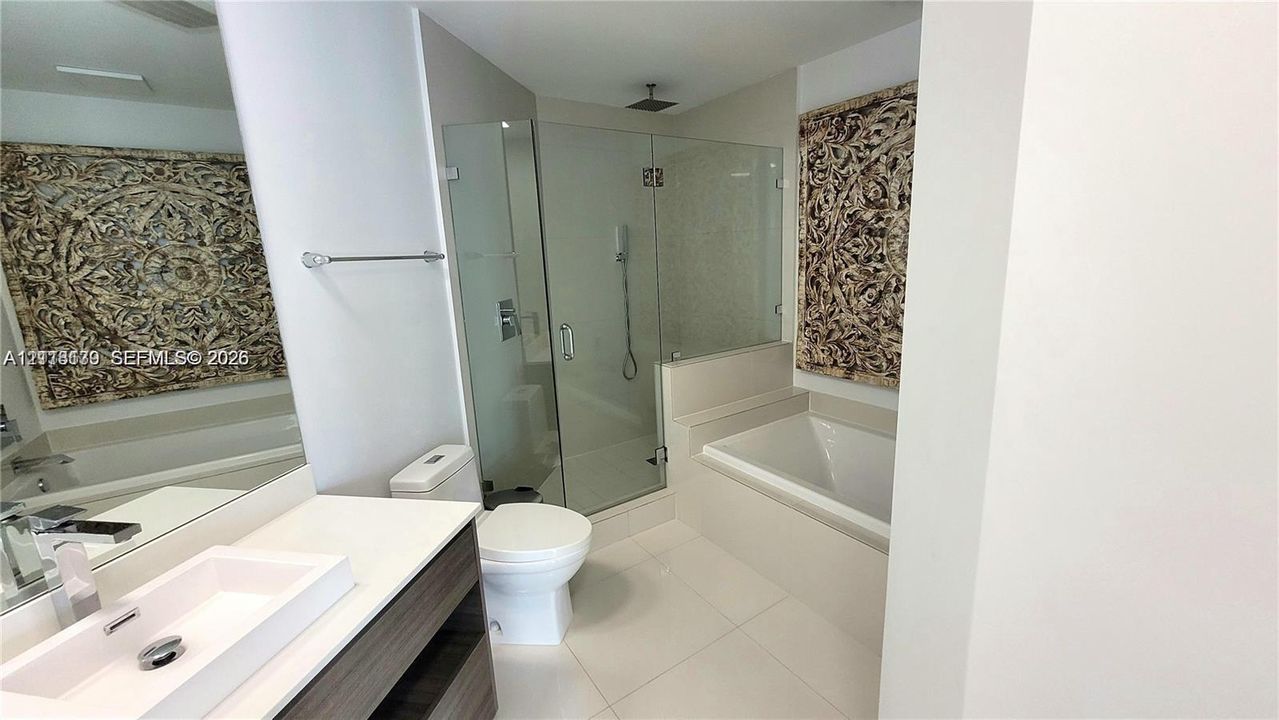 Bathroom featuring a rectangular vessel sink, floating vanity with wood-finish cabinetry, frameless glass-enclosed shower, soaking tub, and large wall-mounted mirror