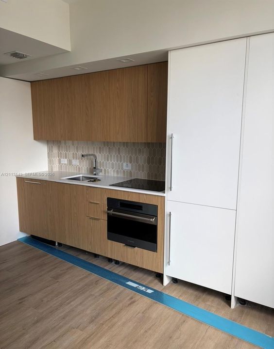Kitchen featuring wood-finish cabinetry, white solid-surface countertops, a textured tile backsplash, a built-in wall oven and cooktop, and a panel-ready refrigerator