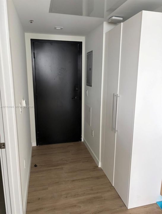 Entryway featuring wood-finish flooring, a matte black door, and built-in floor-to-ceiling cabinetry with stainless steel pulls