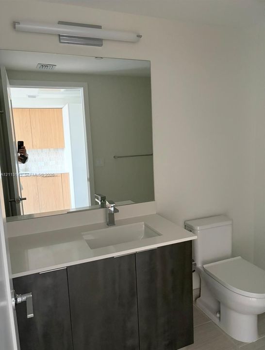 Modern vanity with a rectangular sink, stone-surface countertop, high-contrast cabinetry, large wall-mounted mirror, and linear light fixture