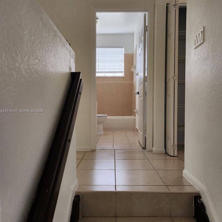 Ceramic tile flooring, dark-finish handrail, built-in shelving, and neutral-toned wall tile surrounding the bathtub enclosure