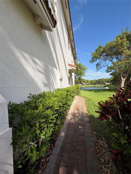 Exterior side walkway featuring paver stones, manicured shrubbery, and waterfront grounds