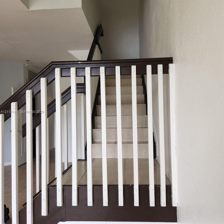Staircase featuring dark wood-finish handrails and contrasting white vertical balusters, complemented by light-toned tile flooring on the steps