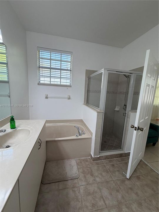 Bathroom featuring a vanity with an integrated sink, a deep soaking tub, and a separate glass-enclosed shower with tiled flooring