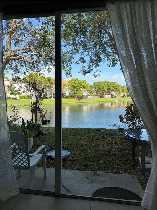 Sliding glass door opening to a concrete patio overlooking a waterfront lot with mature trees