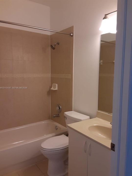 Full bathroom featuring a tub-shower combination with tiled surround, white vanity cabinet with integrated sink, rectangular mirror, and dual-light wall sconce