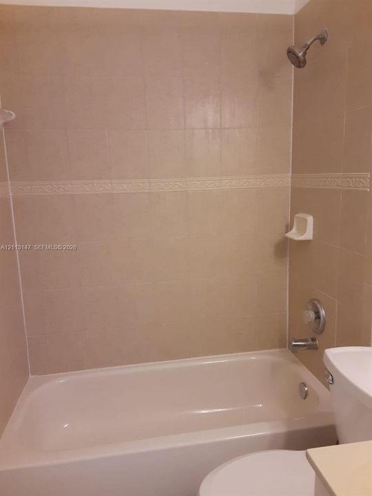 Bathtub with integrated shower, wall-mounted showerhead, built-in soap dish, and decorative tile border