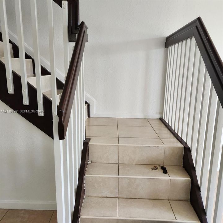 Staircase featuring tiled treads and risers, white vertical balusters, and dark-finish handrails