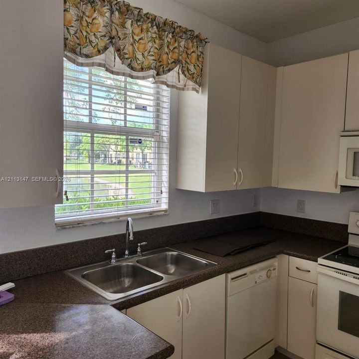Kitchen featuring off-white cabinetry, dark stone-finish countertops, stainless steel double-basin sink with arched faucet, built-in dishwasher, and large window