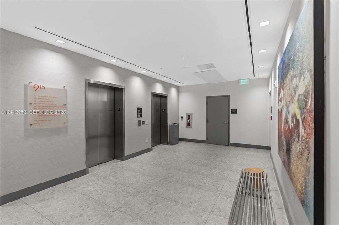 Elevator lobby featuring brushed metal elevator doors, textured wall surfacing, recessed ceiling lighting, and large-format stone-style flooring