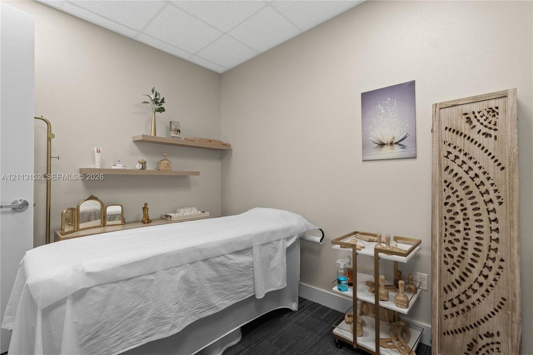 Neutral-toned interior room featuring wall-mounted floating wood shelves, drop ceiling tiles, and dark-toned carpeting