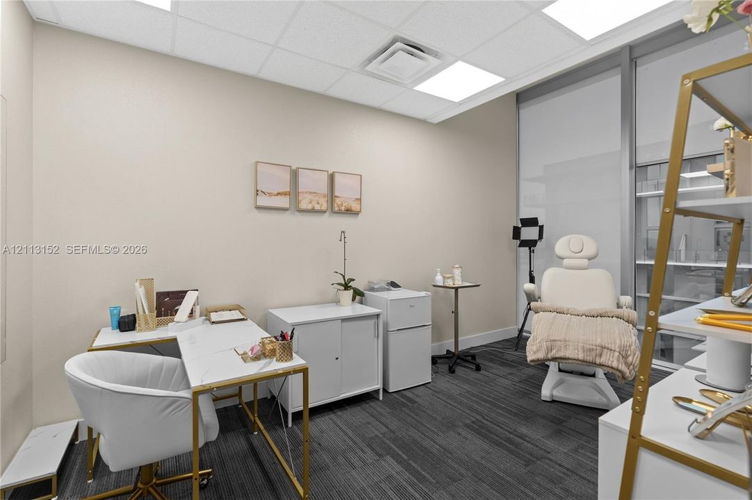 Office space featuring grey patterned carpeting, neutral wall coloring, drop ceiling with recessed panel lighting, and floor-to-ceiling glass wall paneling