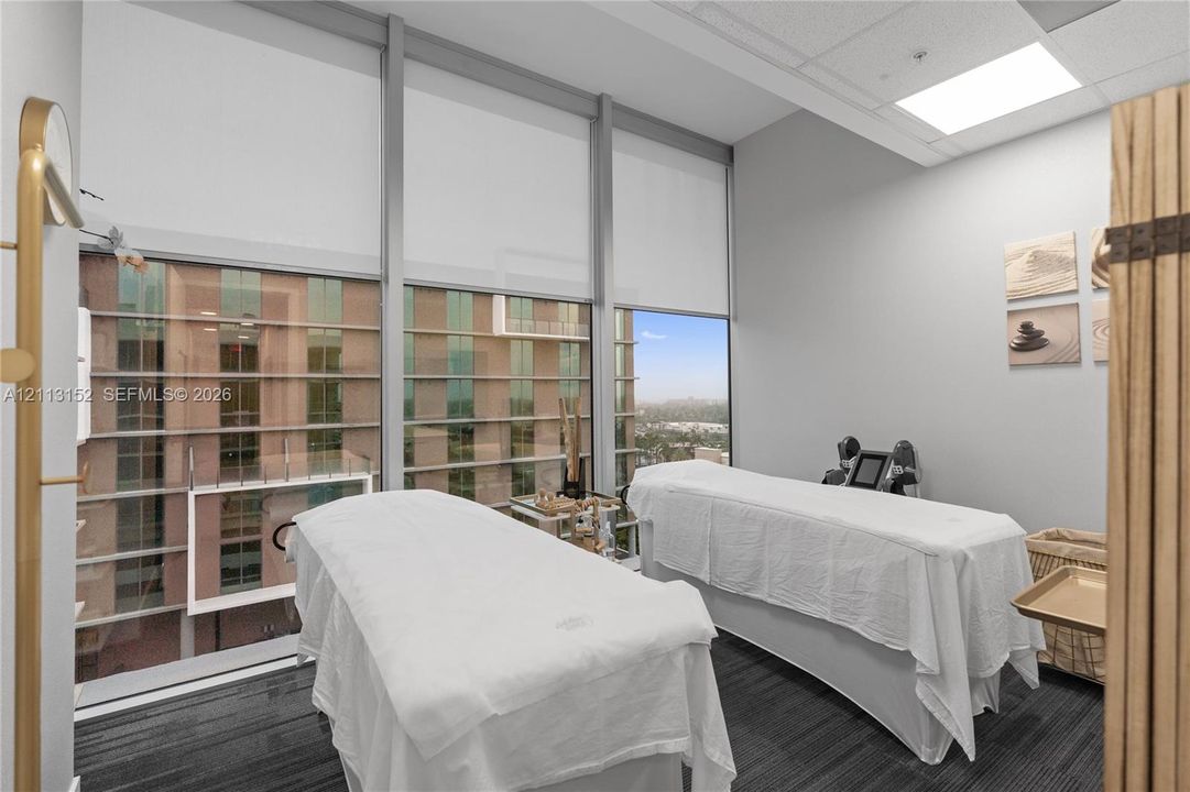 Floor-to-ceiling windows featuring automated roller shades, complemented by neutral wall finishes, drop ceiling panels, and commercial-grade carpet tile flooring