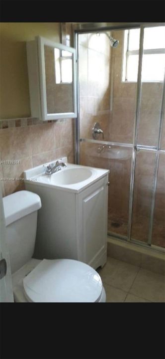 Bathroom featuring a white vanity cabinet with an integrated sink, wall-mounted medicine cabinet, shower enclosure with sliding glass doors, and tiled wall and floor surfaces