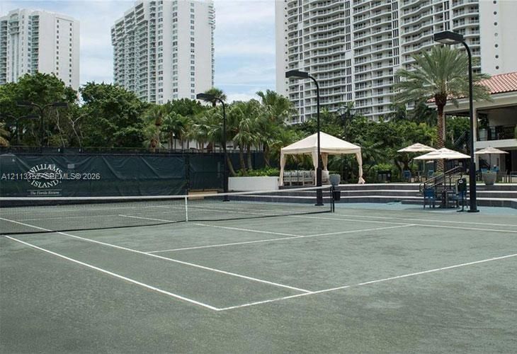 Hard-court tennis facility featuring perimeter lighting, a permanent net system, and tiered concrete spectator seating