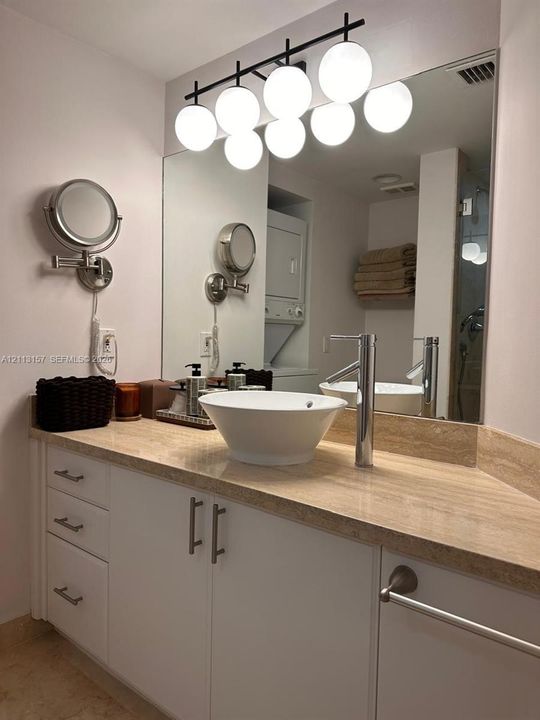 White vanity cabinet with stone countertop, elevated vessel sink, high-arc chrome faucet, and multi-light glass globe fixture