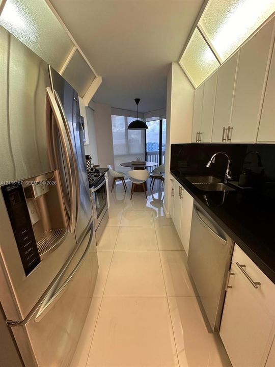 Kitchen featuring white cabinetry with stainless steel hardware, contrasting black countertops, a dual-basin undermount sink, stainless steel appliances, and large-format tile flooring