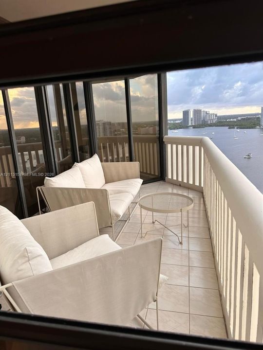 Covered balcony featuring tile flooring, a protective railing, and floor-to-ceiling glass paneling with water and horizon scenery