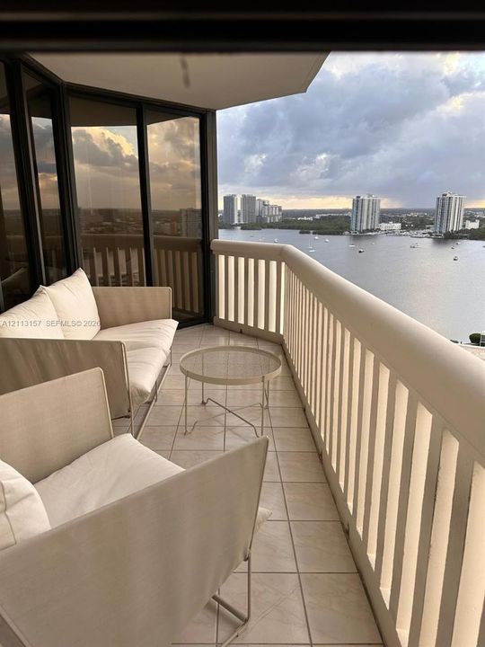 Private balcony featuring tiled flooring, a floor-to-ceiling glass enclosure, and a high-profile structural railing overlooking the water and city skyline