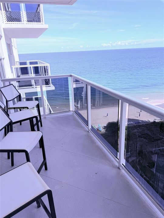 Covered balcony featuring white railings, tempered glass panels, and solid flooring with an ocean backdrop