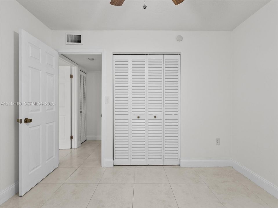 Neutral tile flooring, white six-panel interior doors, and closet featuring white bi-fold louvered doors