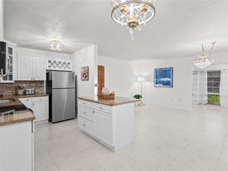 Kitchen featuring white cabinetry with built-in wine rack, stone-finish countertops, stainless steel refrigerator, tile flooring, and decorative multi-light chandeliers
