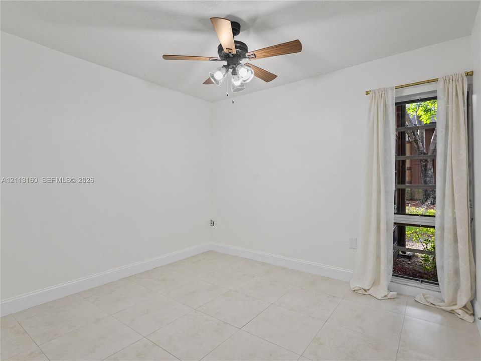 Neutral tile flooring, multi-light ceiling fan with wood-finish blades, and tall window with black-frame muntins
