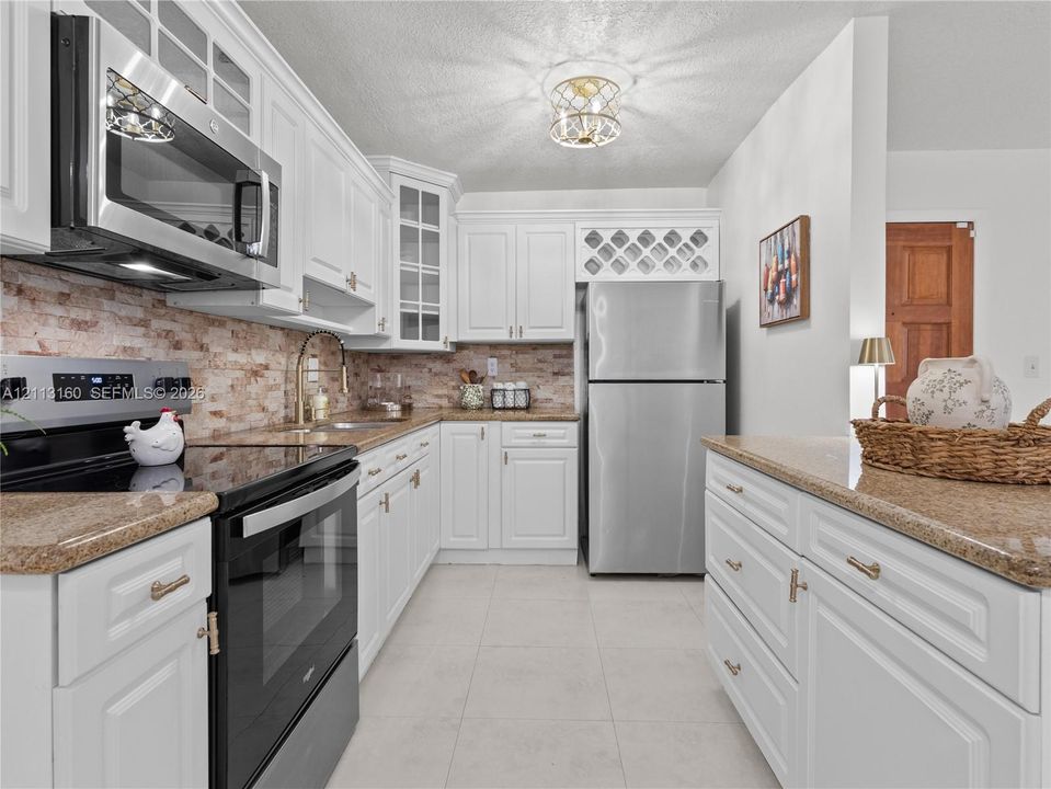 Kitchen featuring white shaker-style cabinetry, stone-finish countertops, stainless steel appliances, brick-style tile backsplash, and a built-in wine rack