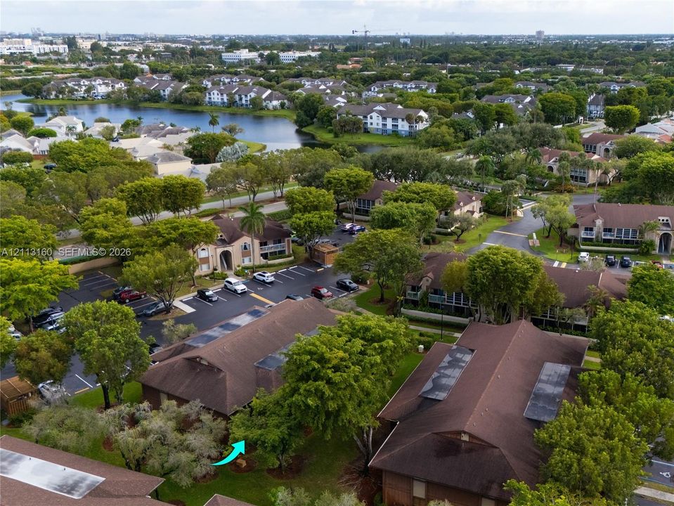 Aerial perspective of multi-family structures featuring brown shingle roofing, integrated skylights, and mature tree-lined landscaping within a planned community setting