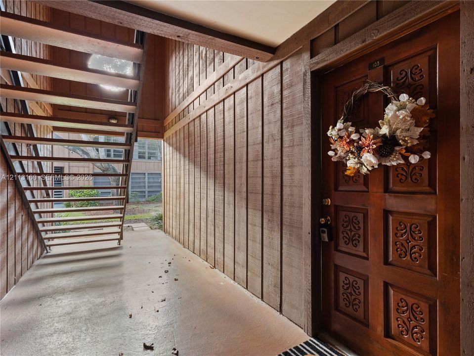 Entryway featuring a decorative wood-paneled door, vertical wood-plank siding, and an open-riser staircase with metal railings