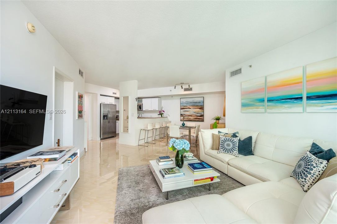 Open-concept living space featuring high-gloss tile flooring, white cabinetry, a built-in kitchen breakfast bar, and stainless steel kitchen appliances