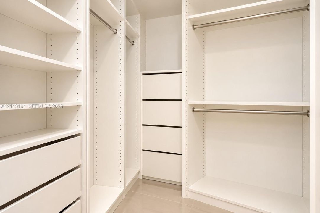 Custom walk-in closet featuring white built-in shelving, integrated dresser drawers, and metal hanging rods