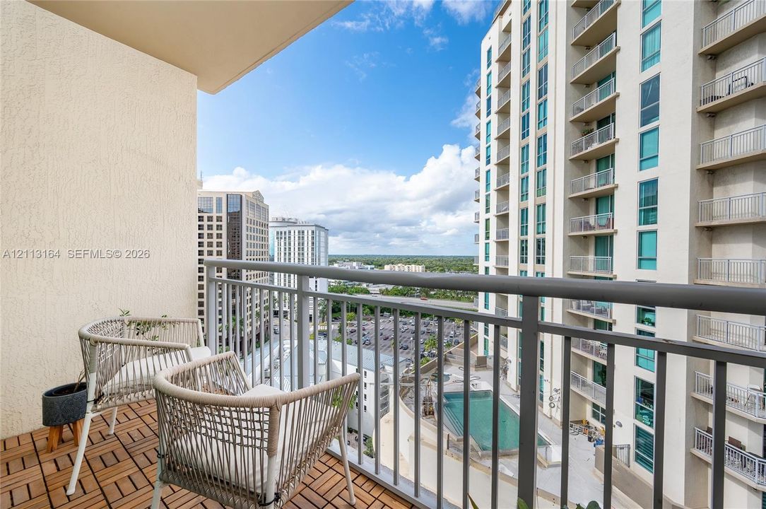 Covered balcony featuring modular wood-tile flooring, metal railing, and urban landscape surroundings