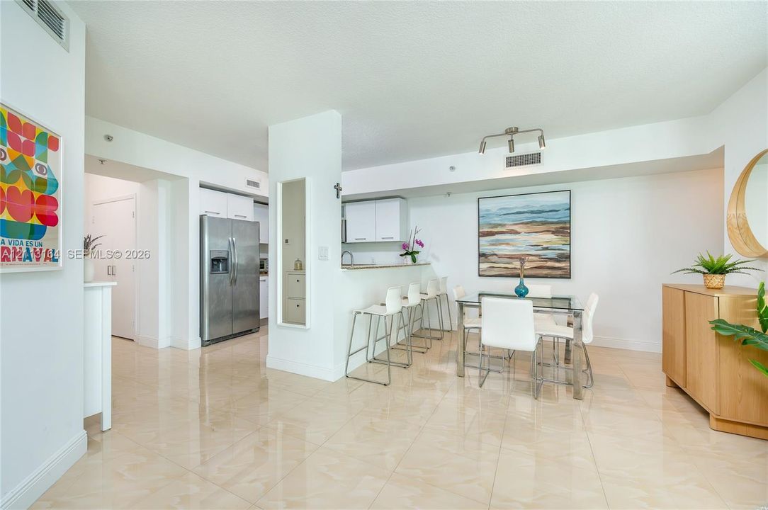 Open-concept kitchen and dining area featuring polished tile flooring, white cabinetry, a stainless steel refrigerator, breakfast bar, and track lighting