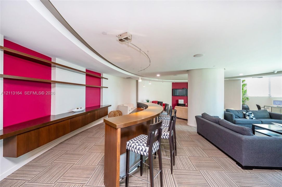 Curved built-in bar, floating wood cabinetry, open-concept floor plan, recessed track lighting, and geometric patterned flooring