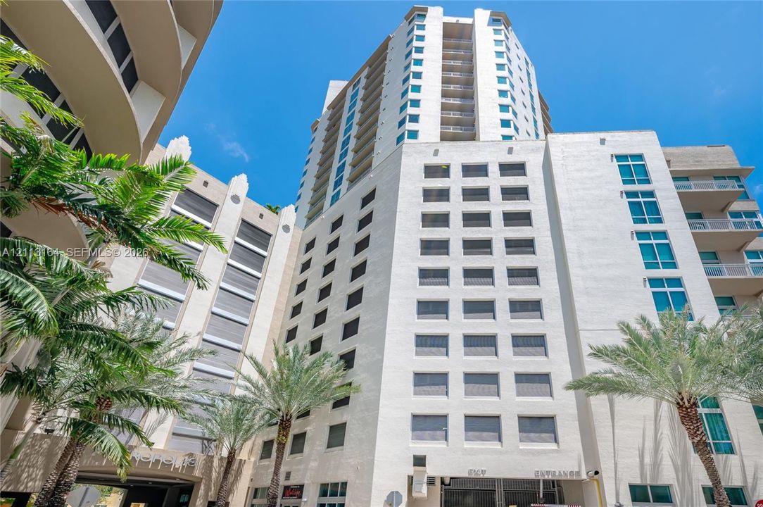 High-rise building featuring a light-toned stucco facade, tiered architectural structure, expansive window placements, private balconies, and integrated landscaping with mature palm trees