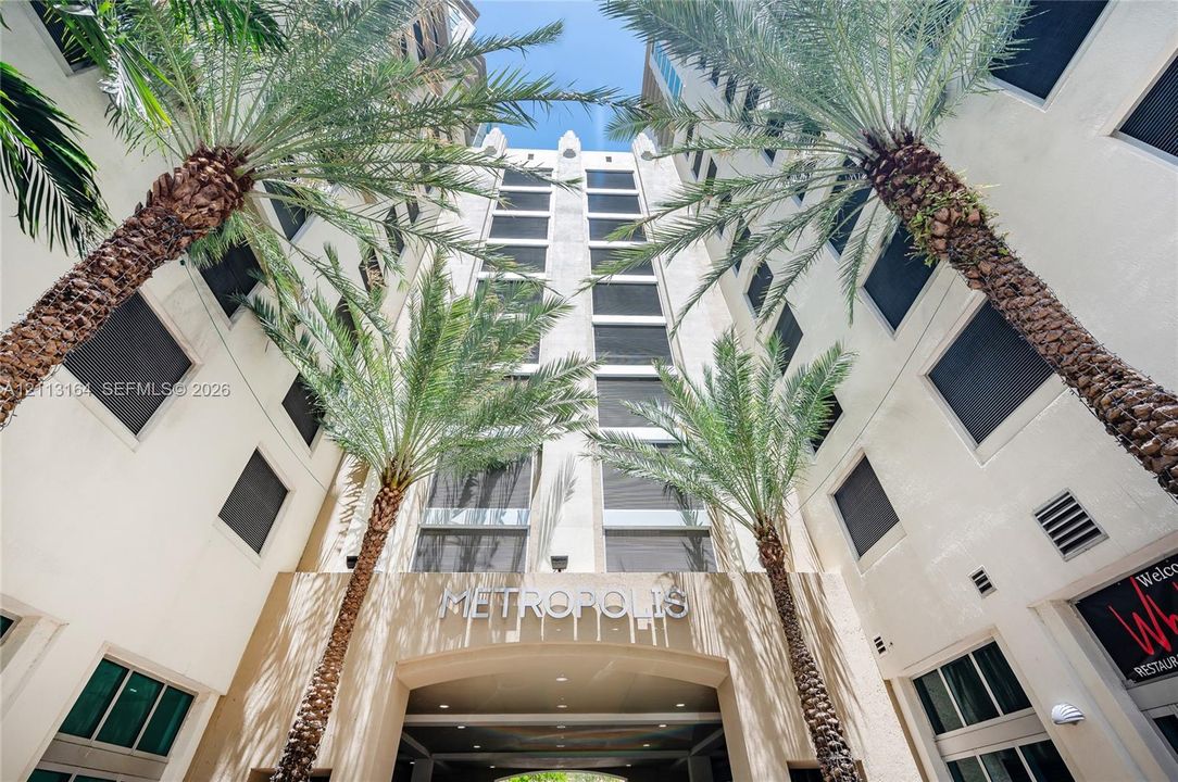 Multi-story high-rise exterior featuring a stucco facade, tiered architectural design, integrated palm trees, and recessed entry